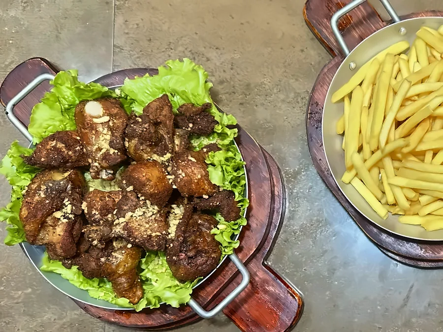 Porção de frango a passarinho e porção de fritas nas tábuas da casa.